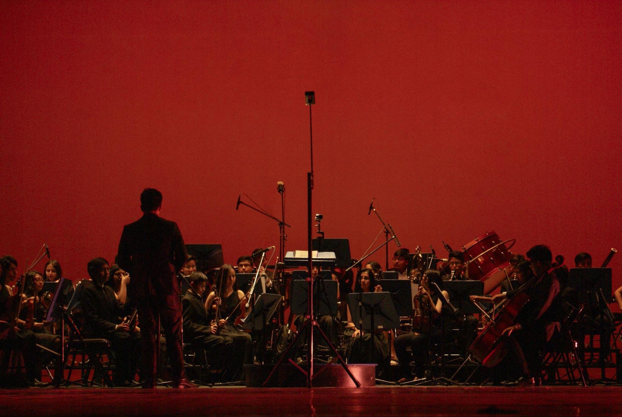 A symphony orchestra performing live on stage under dramatic red lighting.